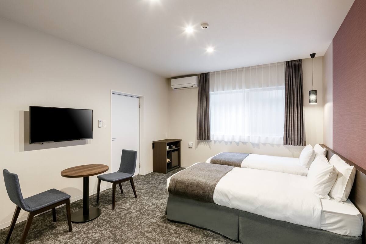 A hotel room with two beds, a TV, a desk, and a chair.