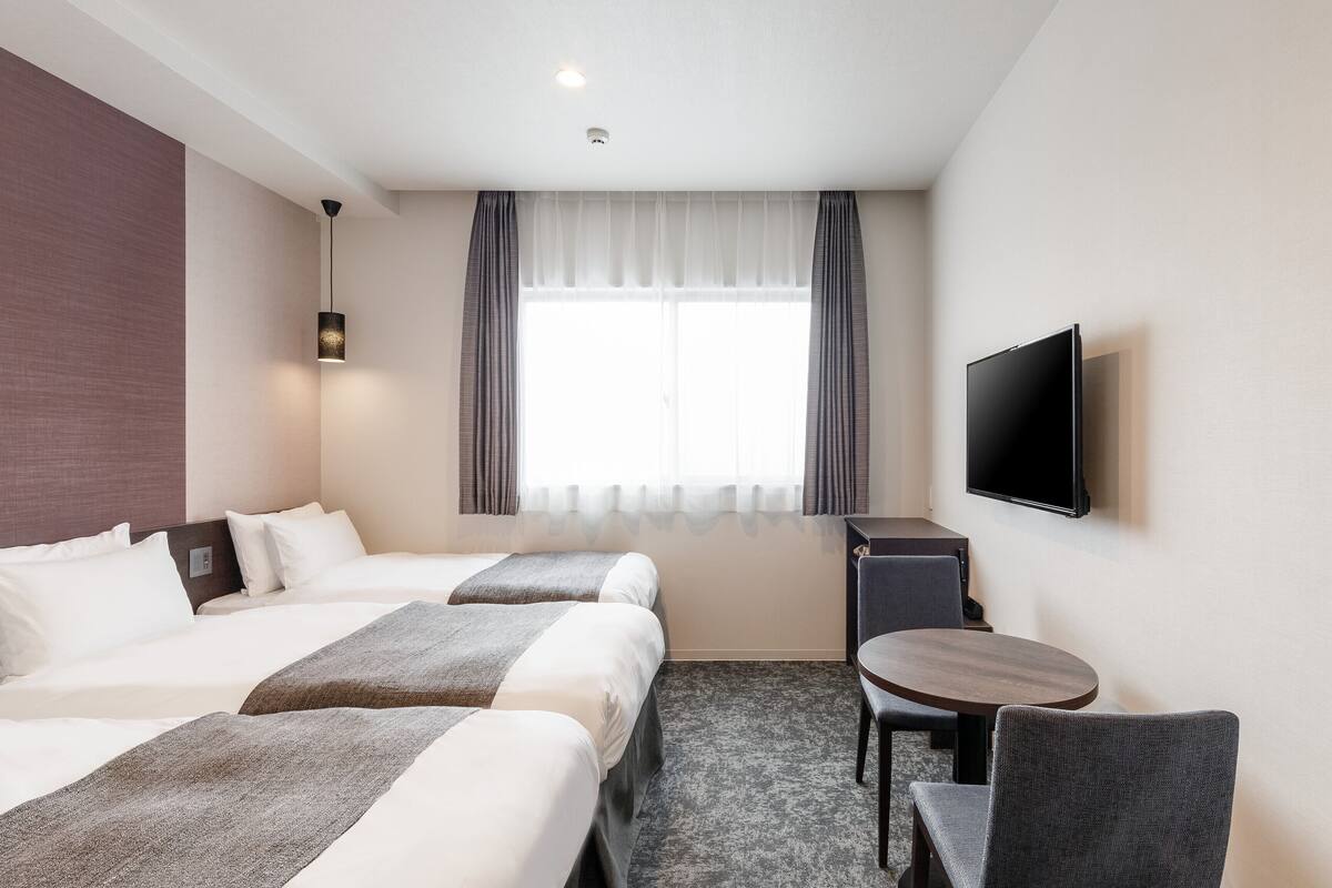 A hotel room with two beds, a desk, a chair, a TV, and a window with curtains.