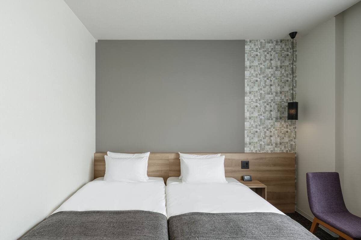 A hotel room with a double bed, a small bedside table, a chair, and a wall with a mosaic tile design.