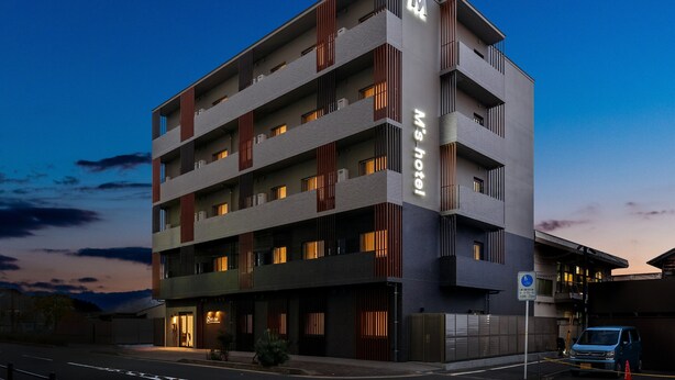 Un hôtel à plusieurs étages, doté d’une architecture moderne, avec des balcons et une enseigne bien visible indiquant « M’s Hotel ».