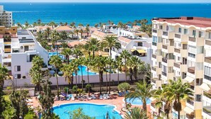 Et resort med flere swimmingpools omgivet af palmer og udsigt til havet.
