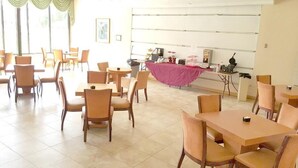 Un espace repas comprenant plusieurs tables et chaises, une table recouverte d’une nappe rose et un comptoir où sont exposés divers articles.