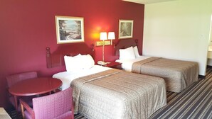 Une chambre d’hôtel avec deux lits, une petite table et deux chaises. Deux lampes sont fixées au mur et des tableaux encadrés sont accrochés au-dessus des lits.