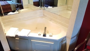 A corner bathroom with a large bathtub, a mirror, and a vanity with a sink. - Red Carpet Inn & Suites (Penns Grove)