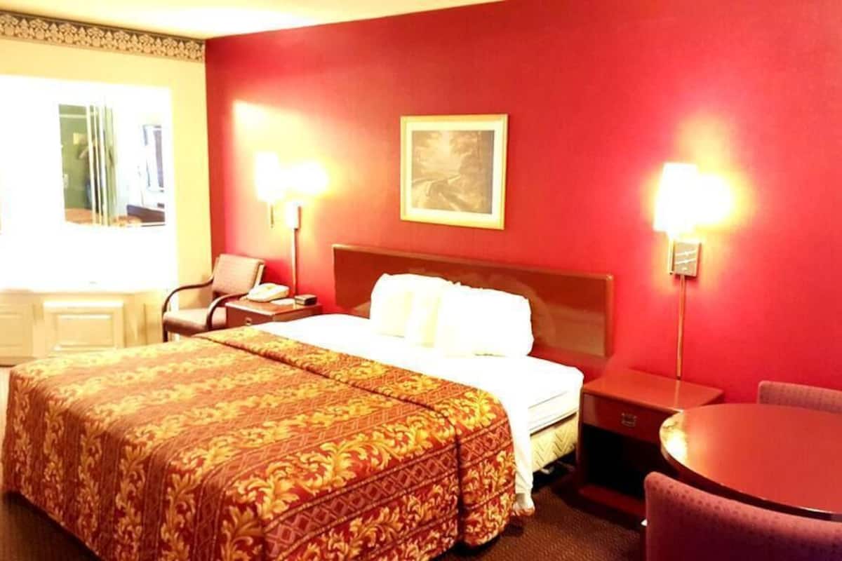 Ett hotellrum med en stor säng, ett skrivbord, en stol och ett litet bord.
