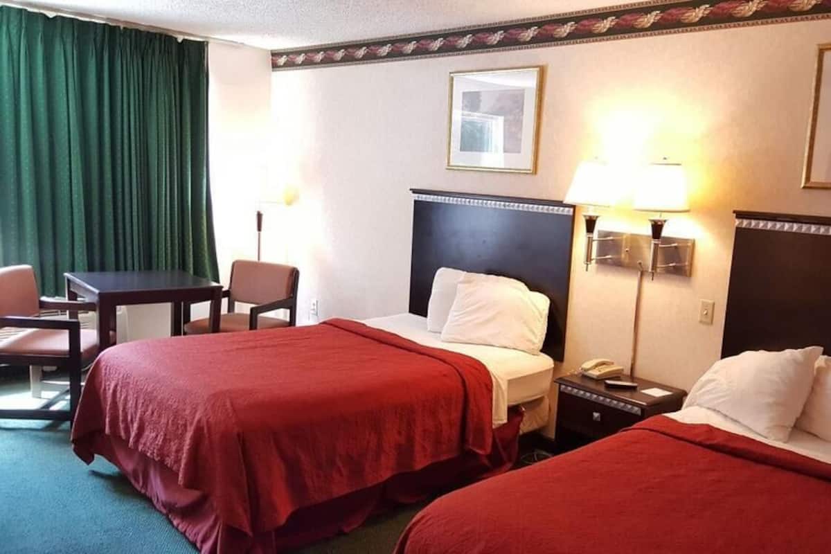 Ett hotellrum med två sängar, ett skrivbord, stolar och ett nattduksbord med en lampa.