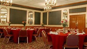Une salle de banquet avec des tables rondes recouvertes de nappes rouges, disposées en rangées.