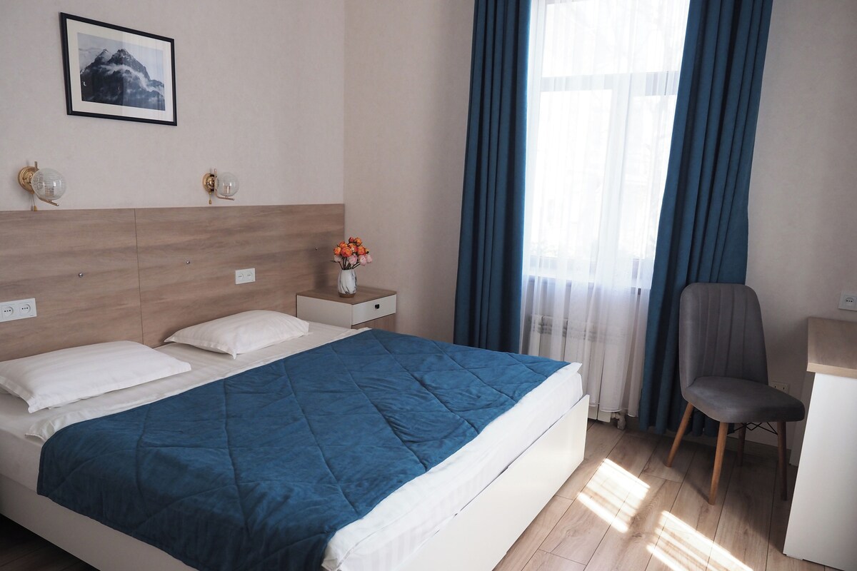 A neatly arranged hotel room with a bed, bedside table, chair, and a window with curtains.