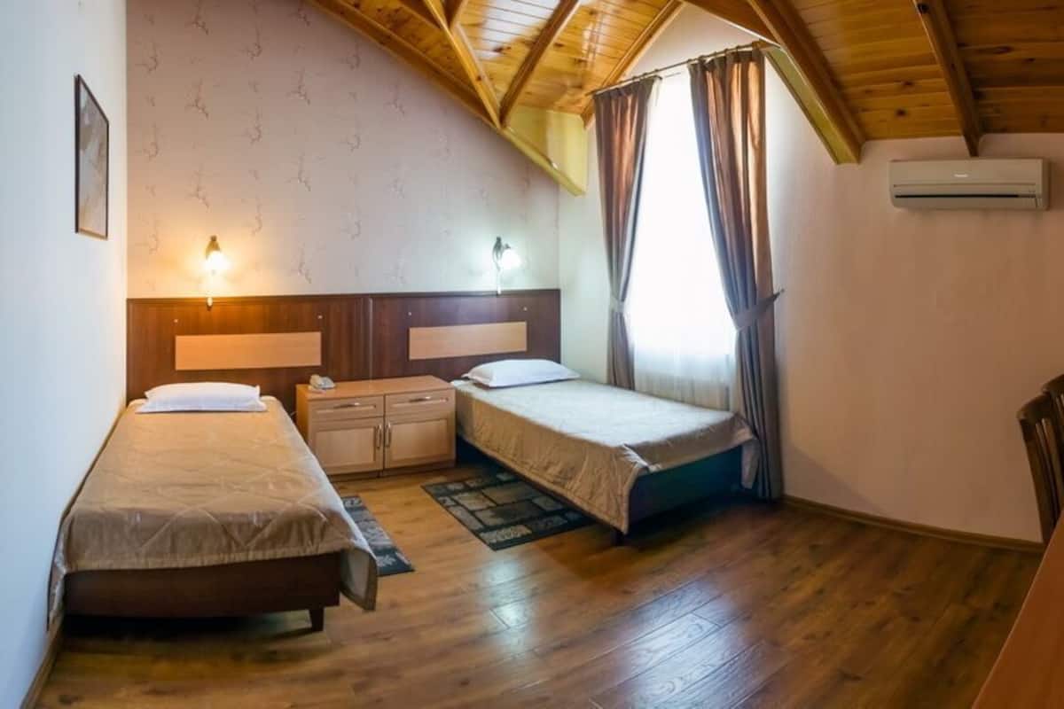 A room with two beds, a wooden ceiling, a desk with a chair, and a television.