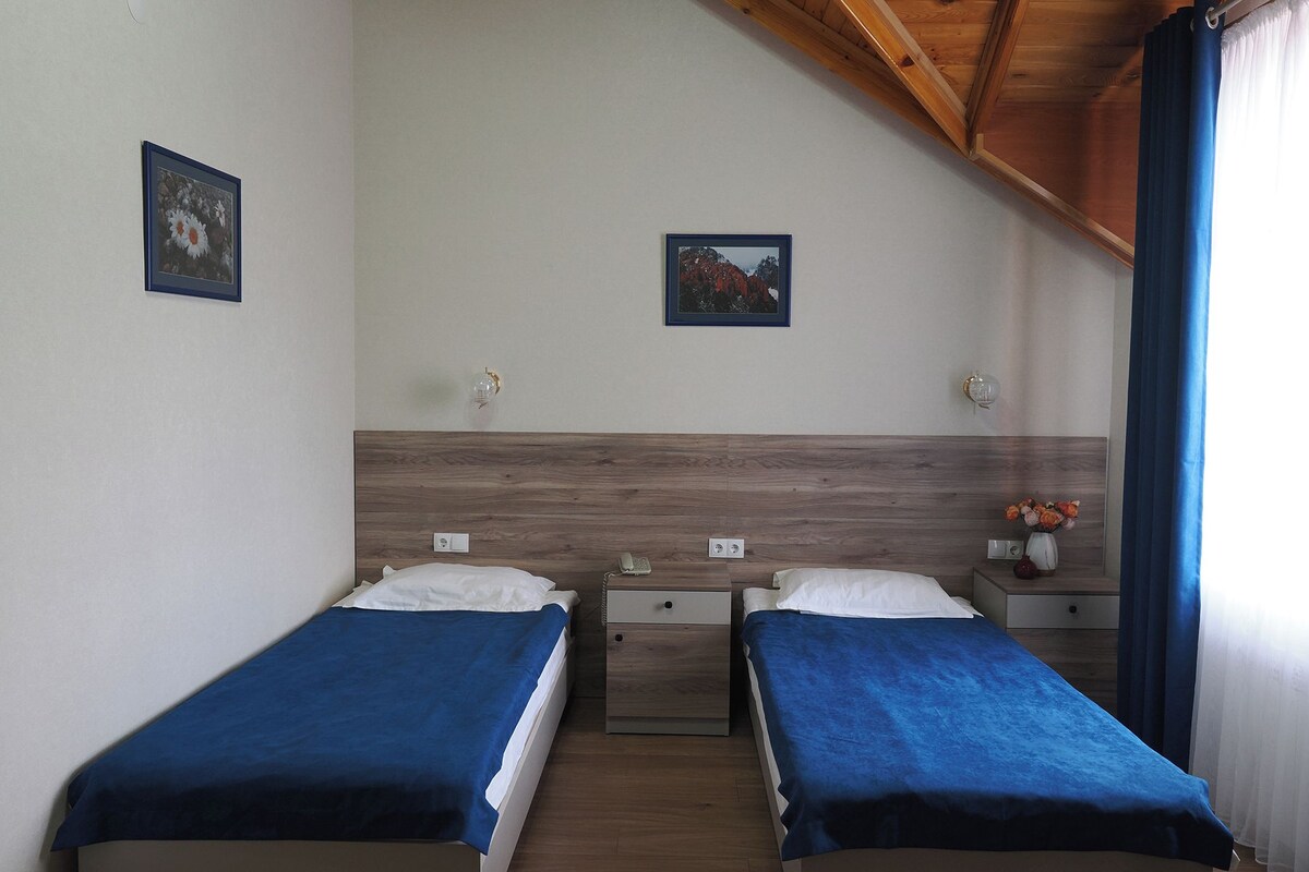 Ein Zimmer mit zwei Betten, Holz-Kopfteilen, einem kleinen Tisch mit Blumenvase und zwei gerahmten Bildern an der Wand.