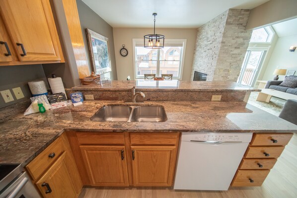 A kitchen with granite countertops, wooden cabinets, a double sink, and a dishwasher. - Updated Townhome | Deck w/Mountain Views, Hot Tub (Keystone)