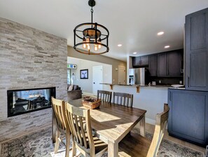 A modern kitchen with dark cabinets, a stainless steel refrigerator, and a dining area with a wooden table and chairs.