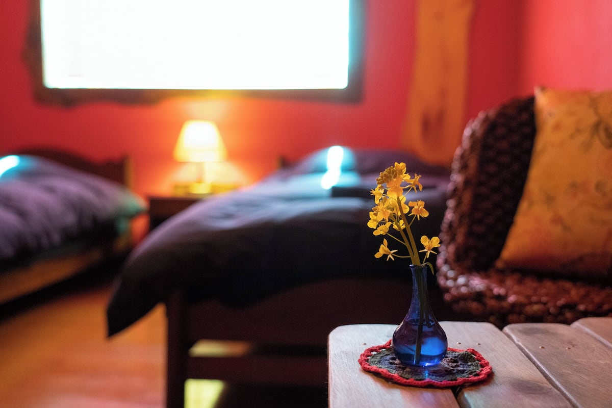 A room with a bed, a bedside table with a vase of flowers, and a lamp.