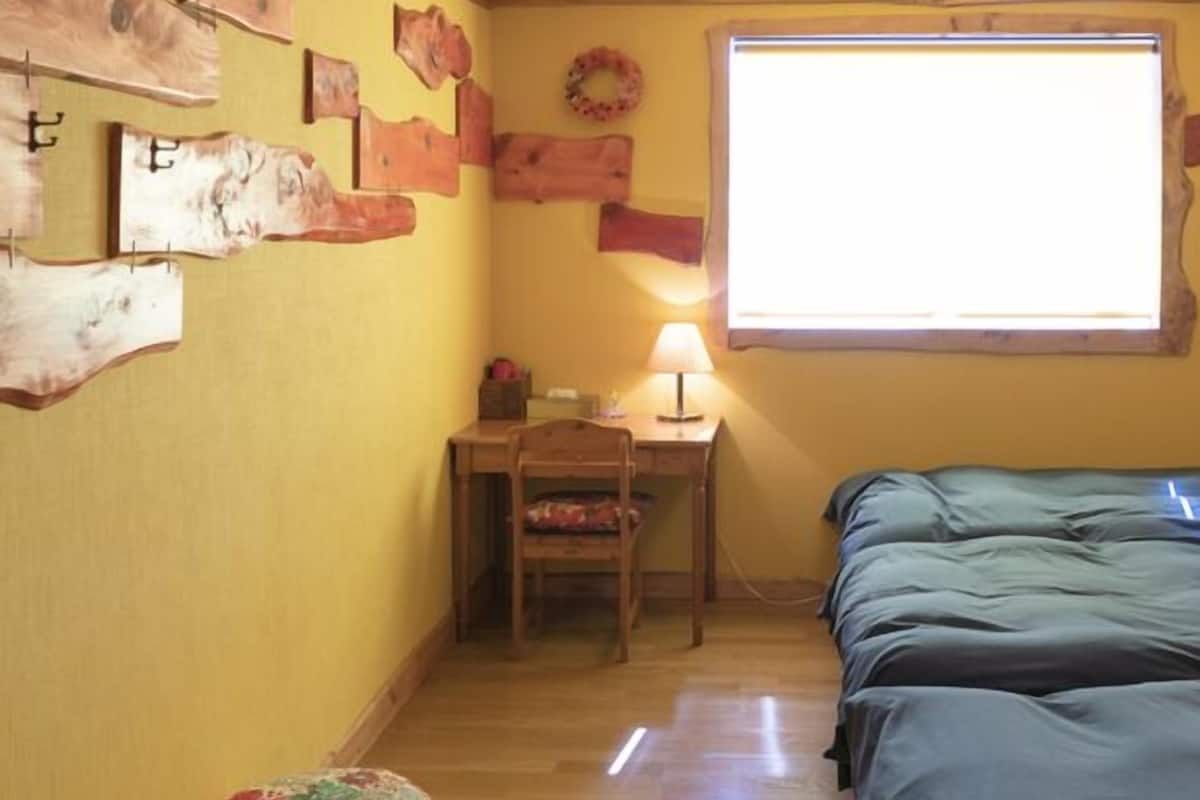 Quarto pequeno com cama, escrivaninha e cadeira, janela e parede decorada com peças de madeira.