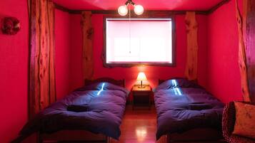 A room with two beds, a wooden floor, a window with a view, and a hanging light fixture.
