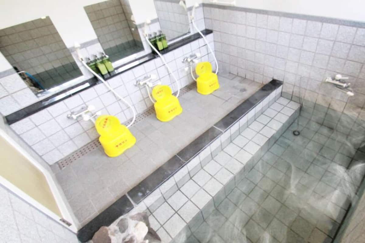 A bathroom with a glass-enclosed shower, a sink with a mirror, and two yellow soap dispensers.