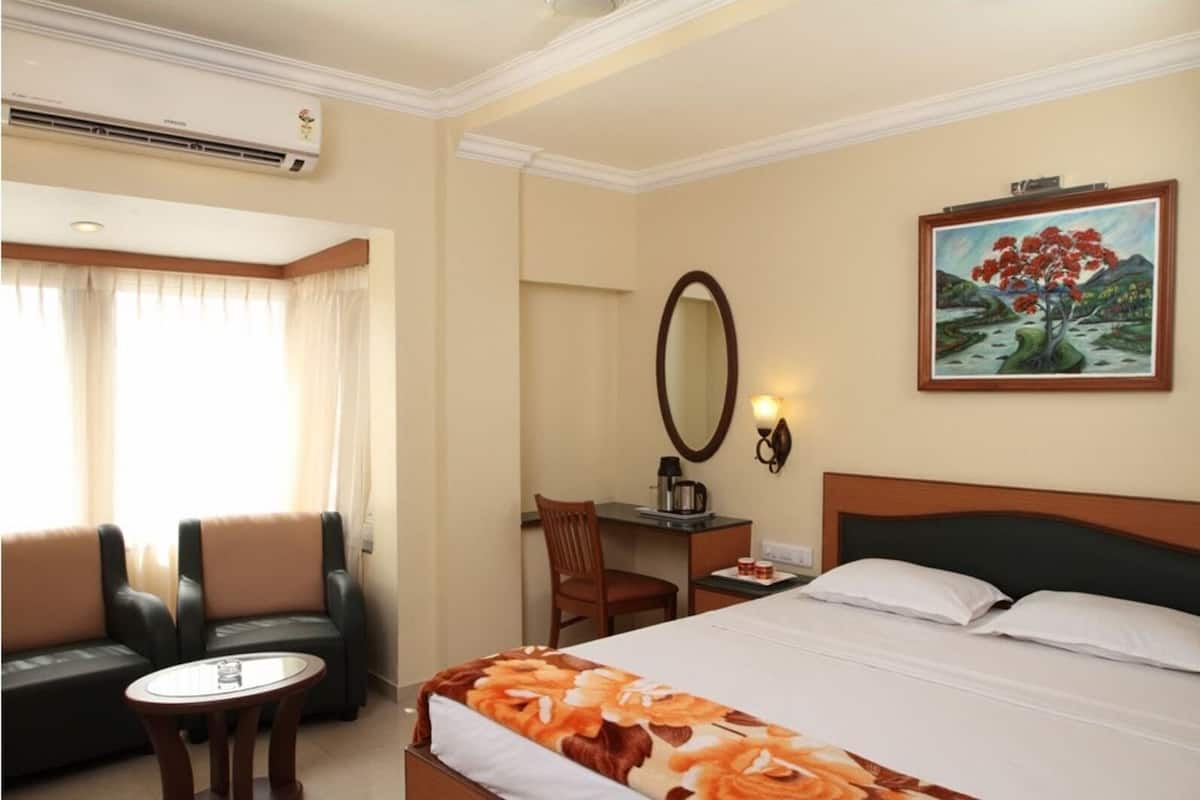 Habitación de hotel con cama, escritorio, silla, sofá, mesa redonda, aire acondicionado, un cuadro y espejo.