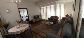 A living room with a sofa, armchairs, a TV, a coffee table, and a dining table with chairs.