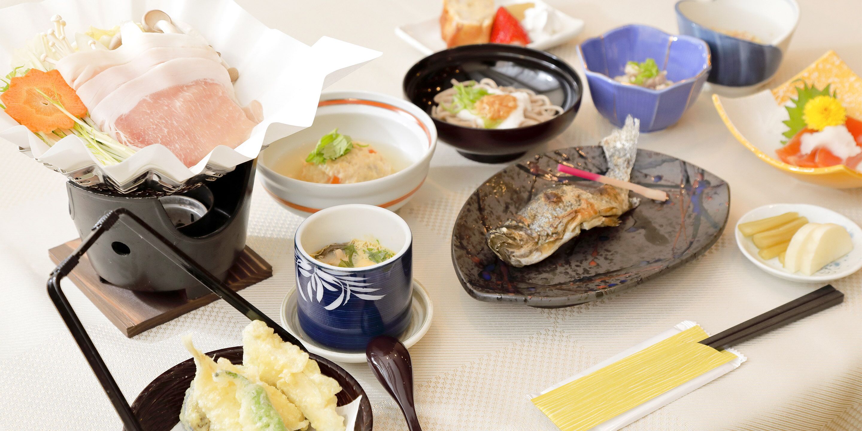 Verschiedene japanische Gerichte, darunter Sushi, Sashimi und Tempura, serviert auf traditionellem Keramik- und Lackgeschirr.
