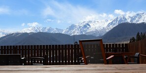 Terraza de madera con muebles de exterior, cerca de madera y montañas al fondo.