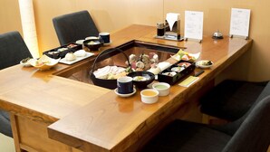 A wooden dining table with various dishes and a hot pot centerpiece, surrounded by black chairs. - Hotel Granjam Tsugaike (Otari)