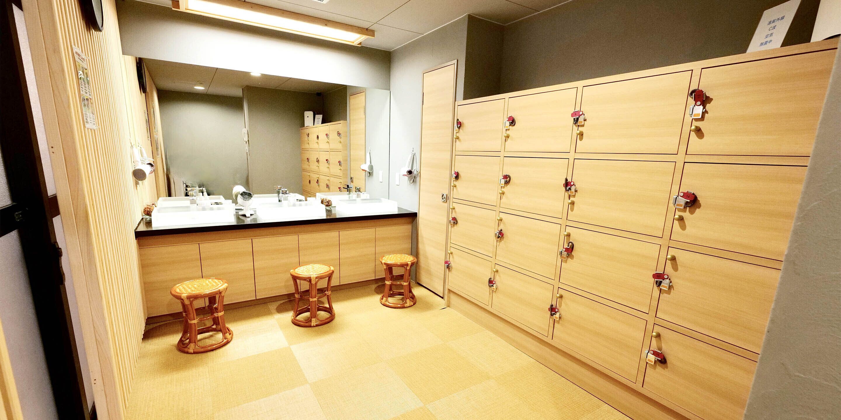 A hotel bathroom with wooden lockers, a large mirror, and three stools.