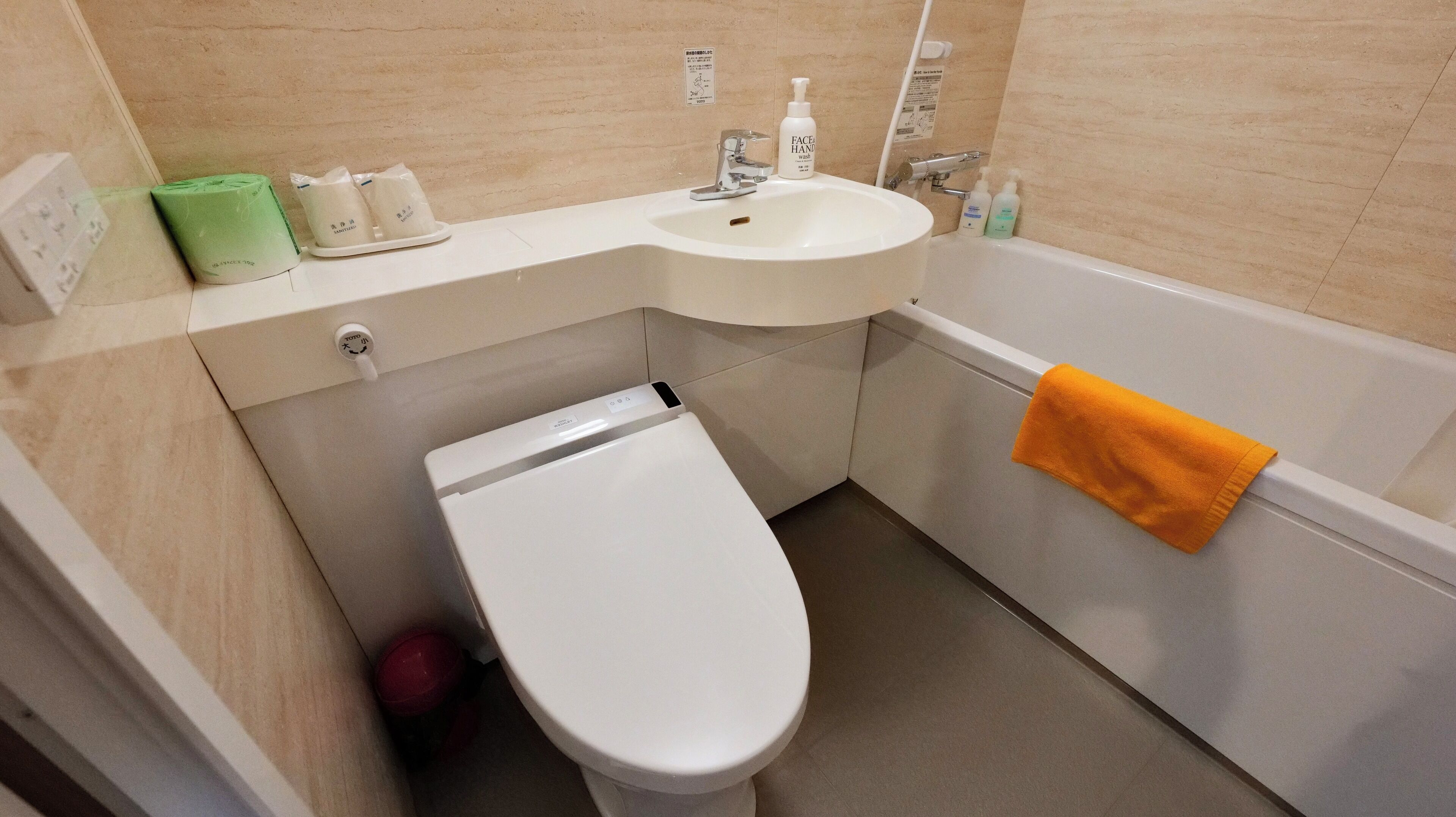 A bathroom with a toilet, sink, and bathtub. There are toiletries on the sink and a towel hanging on the bathtub.