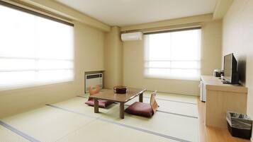 Una habitación con suelo de tatami, una mesa baja con cojines, un calentador y un televisor sobre un soporte.