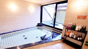 A spa area with a glass-enclosed hot tub, tiled walls, and a shelf with toiletries. - Hotel Granjam Tsugaike (Otari)