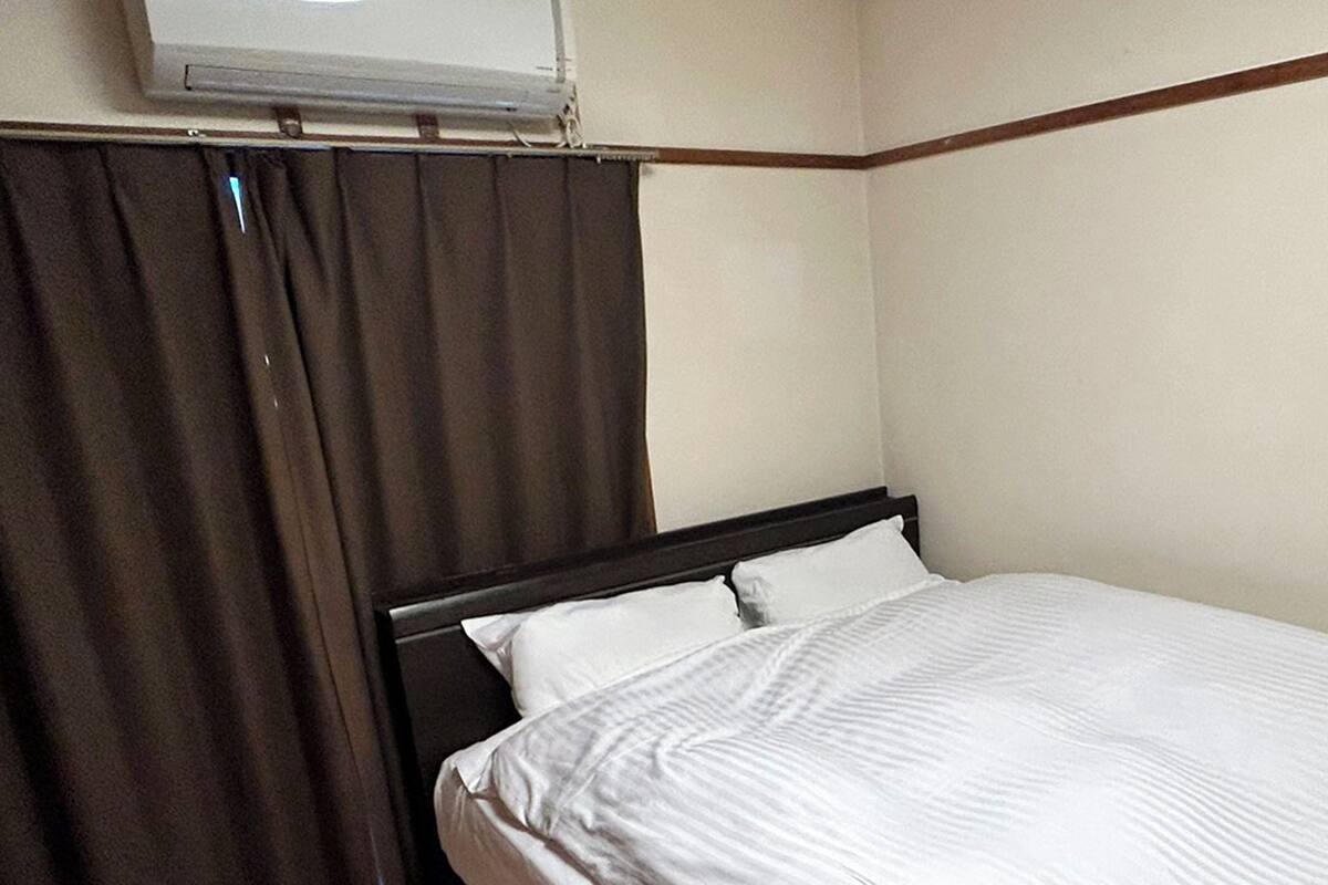 A single bed with white bedding in a room with a wooden headboard and a window with curtains.
