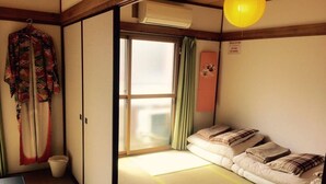 A traditional Japanese room with tatami flooring, a futon bed, a sliding door, and a hanging garment. - Casa Viento Stay Inn (Hiroshima)