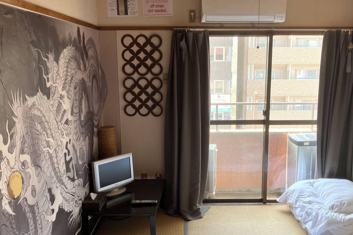 A hotel room with a large window, a bed, a TV on a small table, and a decorative wall piece.