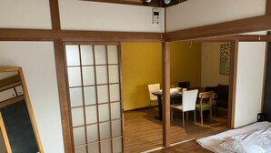 A traditional Japanese room with tatami flooring, a sliding shoji screen, a futon bed, and a dining area visible through the screen. - Casa Viento Stay Inn (Hiroshima)