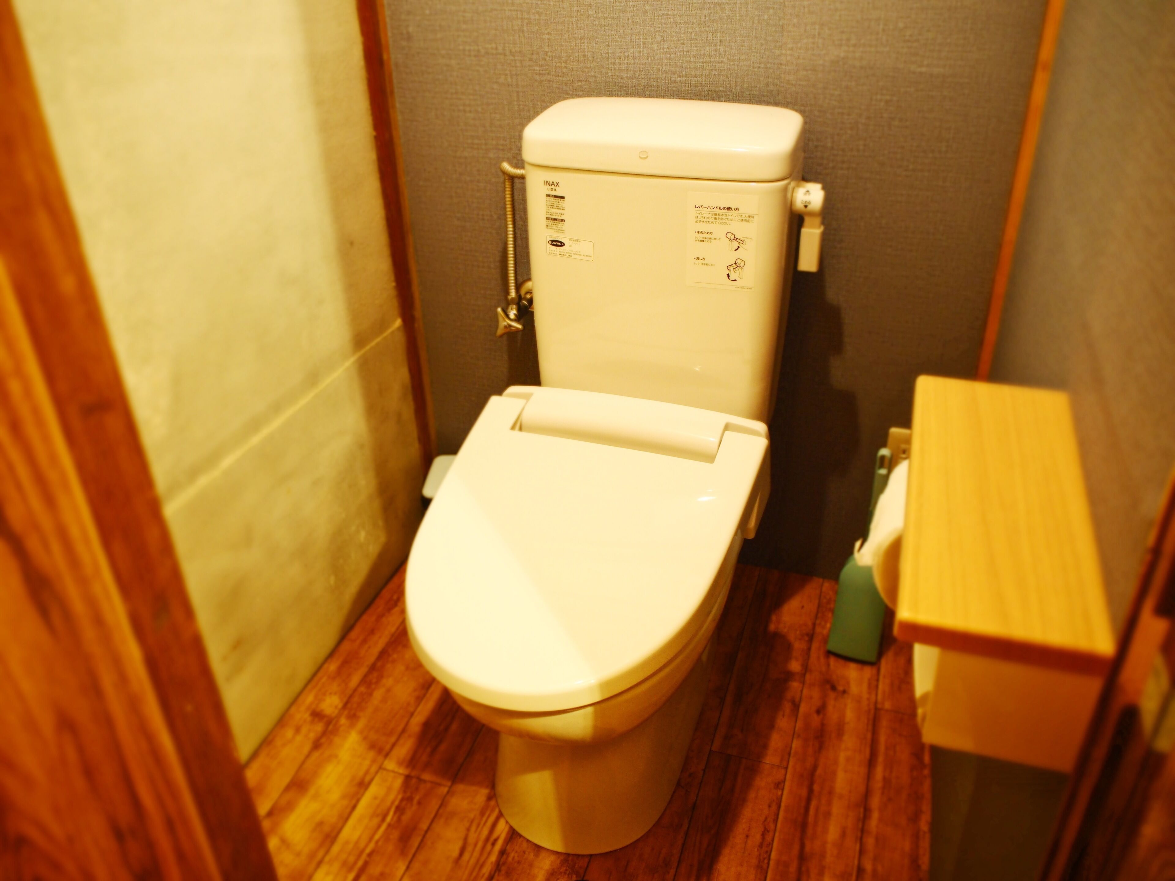 Un inodoro estándar con tanque y asiento, ubicado en un baño pequeño con piso de madera.