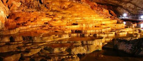 Una grotta con formazioni minerali stratificate e un corpo d'acqua.