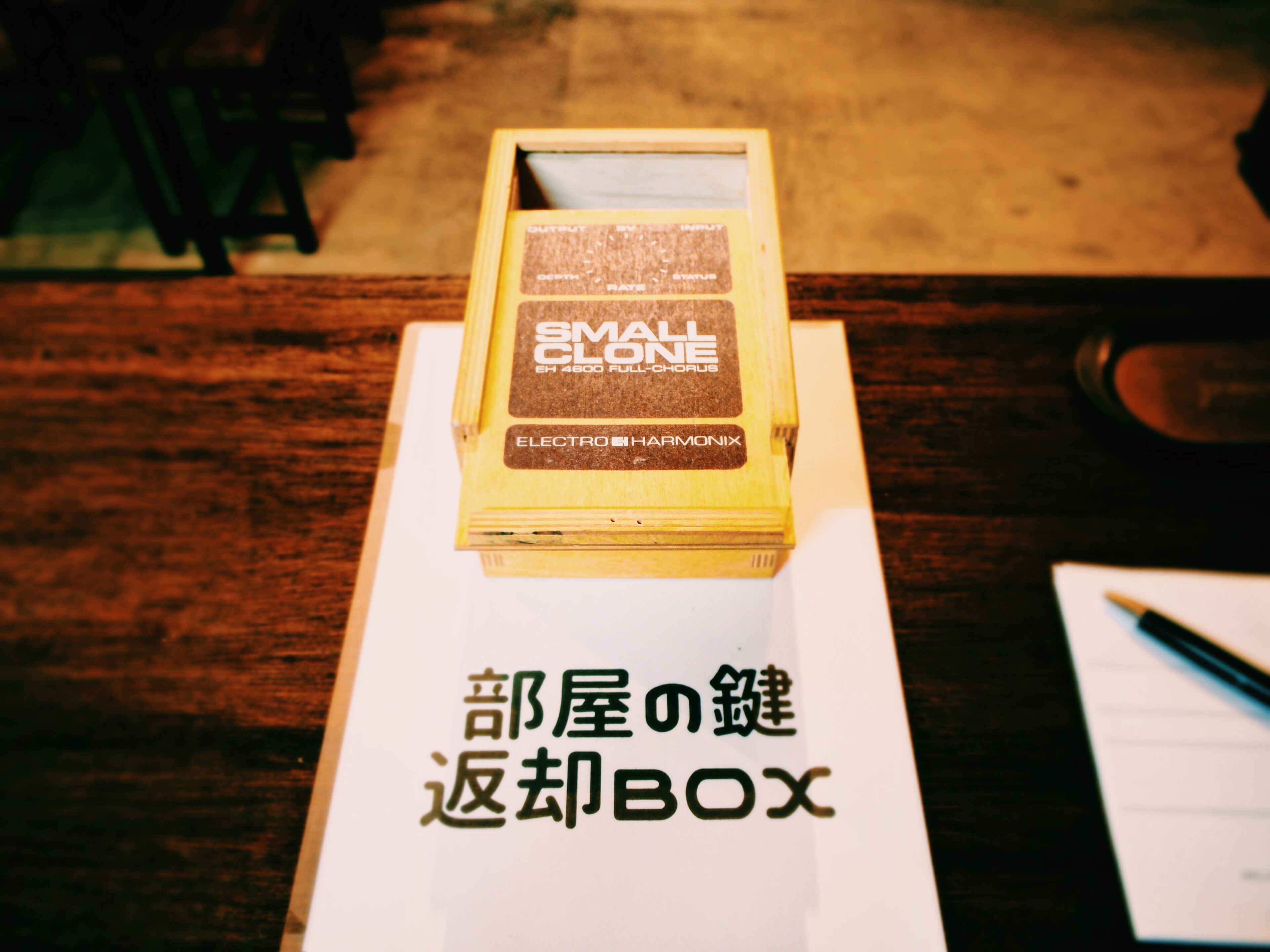 Una mesa de madera con una caja etiquetada "SMALL CLOSENESS ELECTRO HARMONIX" y un papel con texto japonés.