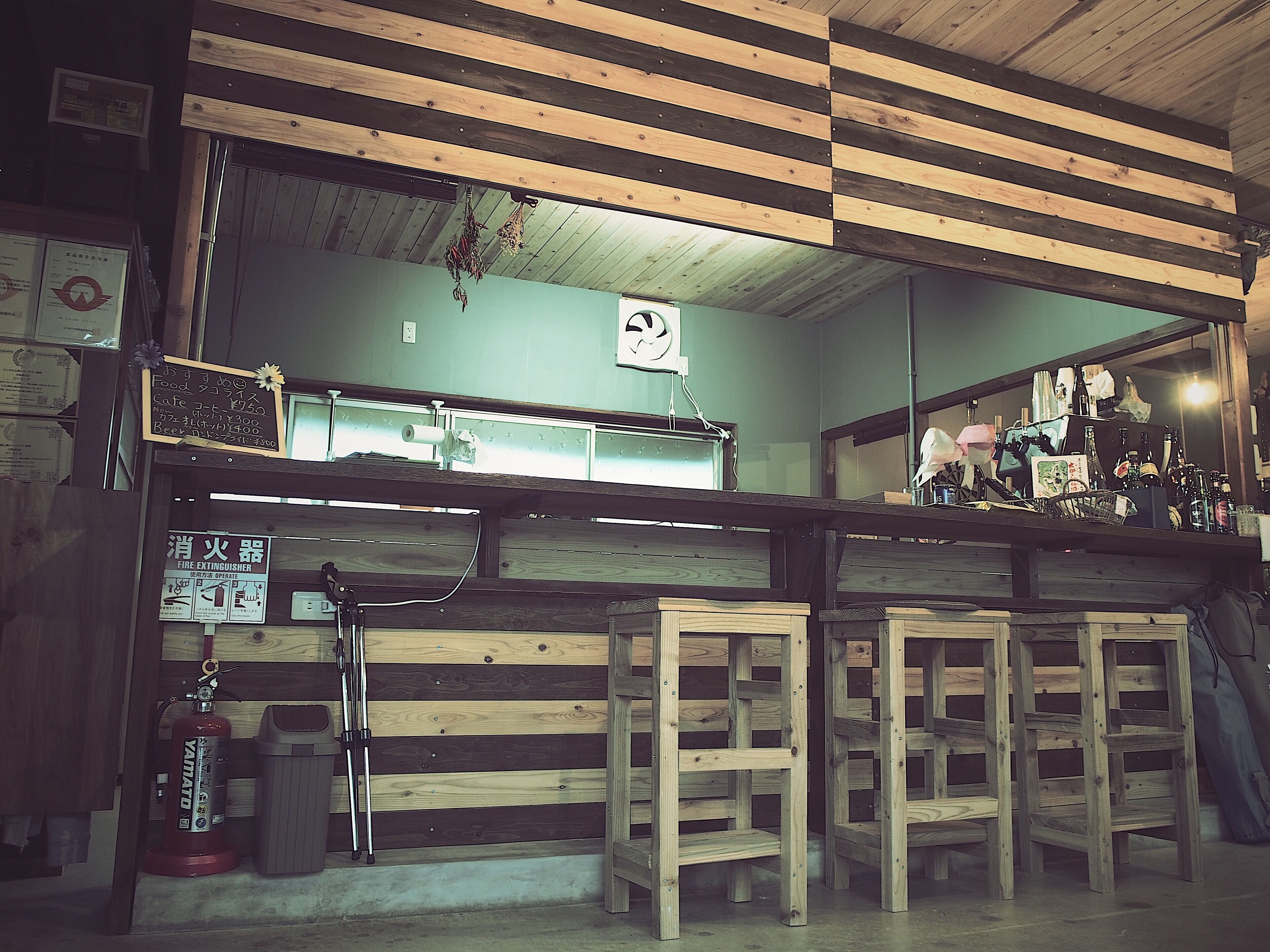 Zona de bar con vigas de madera, un extintor y un ventilador de techo.