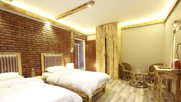 A hotel room with two beds, a wooden wardrobe, a small round table with chairs, and a desk with a chair. - Silu Homes (Lalitpur)