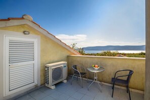 A balcony with a white door, an air conditioning unit, two chairs, and a small table with a bowl of fruit. - Holiday house TRSJA with swimming pool (Linardići)