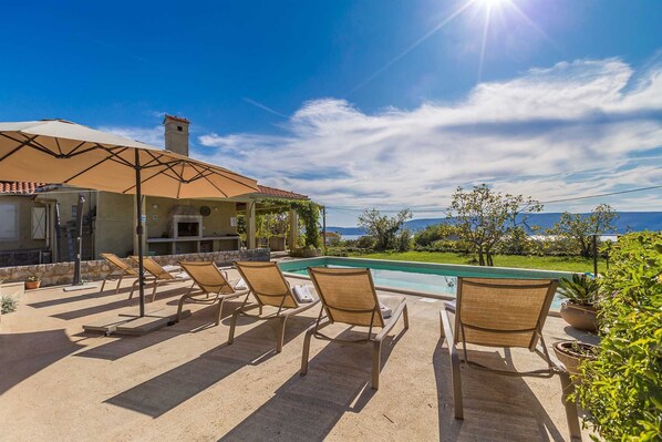 A poolside area with lounge chairs, a barbecue, and a view of the sea. - Holiday house TRSJA with swimming pool (Linardići)