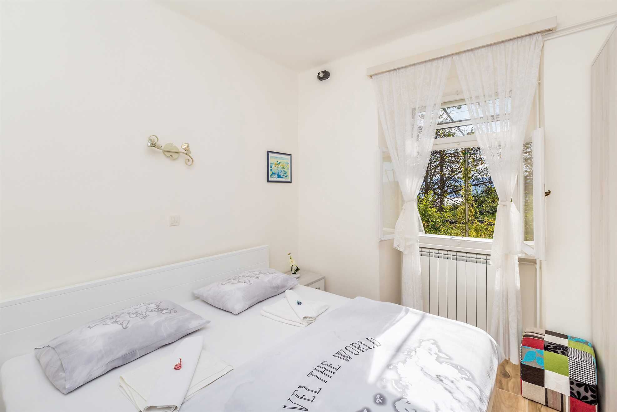 Une chambre à coucher avec un lit, des oreillers, un tableau encadré et une fenêtre avec des rideaux.