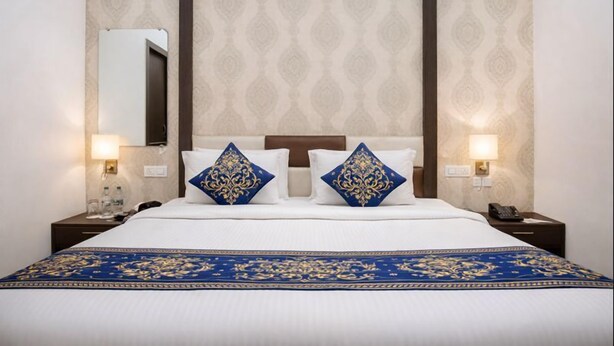 A hotel room with a large bed, two decorative pillows, a nightstand with a phone, and a mirror on the wall. - Hotel Tamanna 2 Minute Walk from Golden Temple (Amritsar)