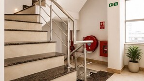 A modern staircase with metal railings, a fire exit sign, and a fire extinguisher on the wall. - Hotel Tamanna 2 Minute Walk from Golden Temple (Amritsar)