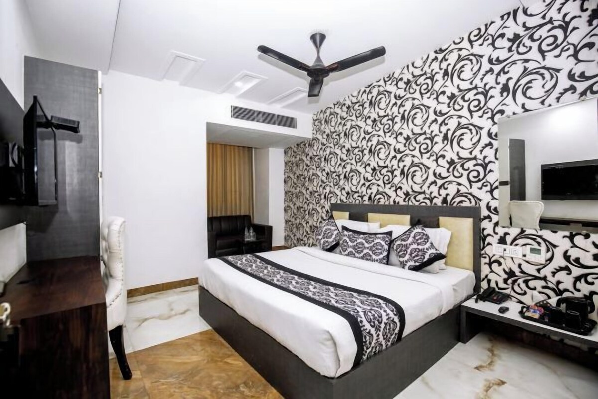 A modern bedroom with a large bed, a ceiling fan, a patterned wallpaper, and a TV on the wall.