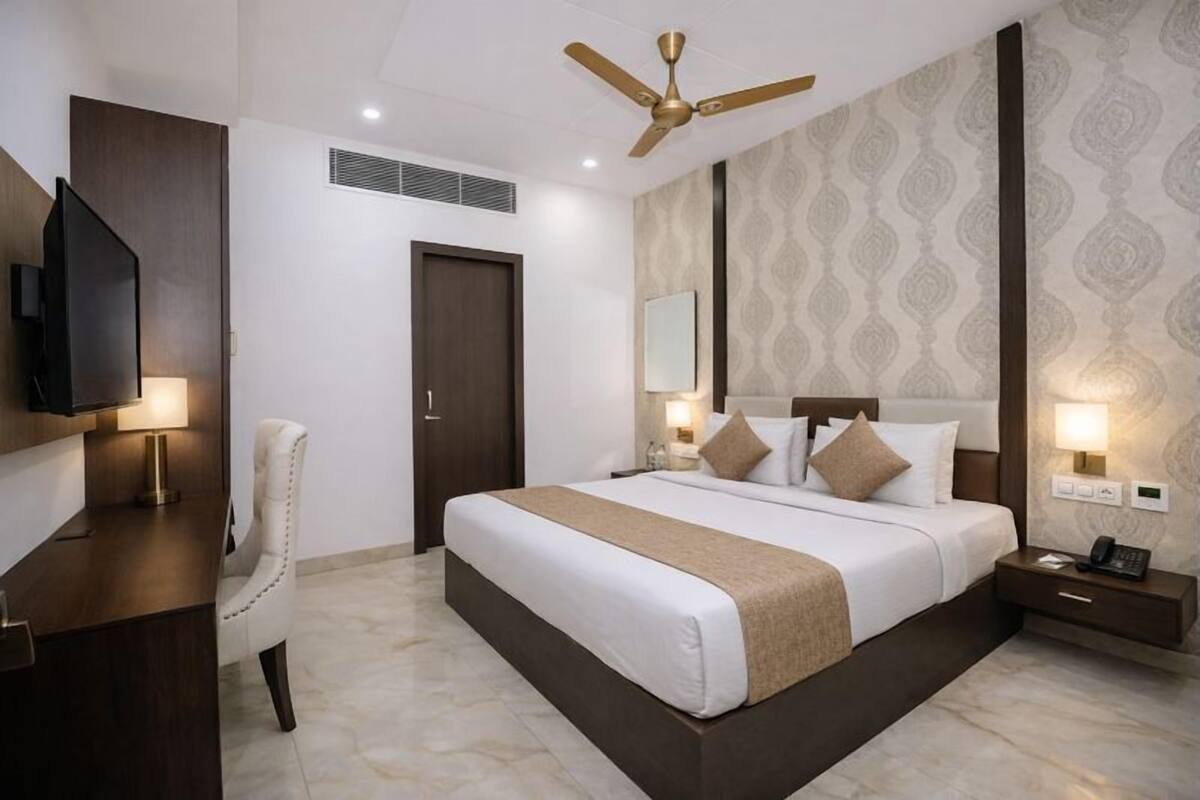 Una habitación de hotel con una cama grande, un escritorio, una silla, un televisor, un ventilador de techo y un papel tapiz estampado.