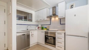 Una cocina moderna con armarios blancos, lavavajillas de acero inoxidable, horno y refrigerador.