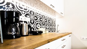 A kitchen with a wooden countertop, a coffee maker, a kettle, and a patterned backsplash.