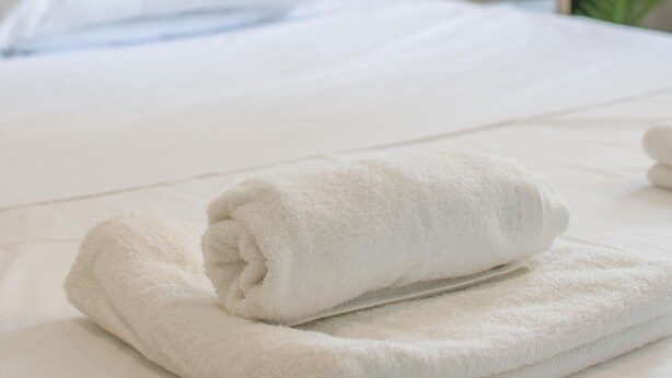 A neatly made bed with white linens and a folded white towel on the side.