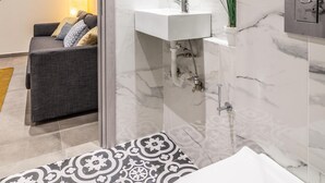 A modern bathroom with a marble wall, a white sink, and a glass shower enclosure.