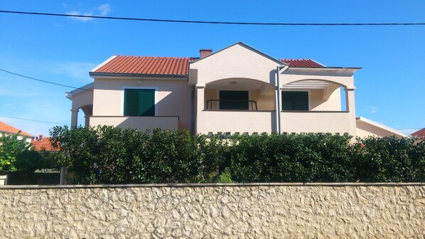 Ein zweistöckiges Haus mit rotem Ziegeldach, einer steinernen Fassade und grünen Fensterläden.